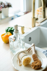 Plate with an ecobrush for washing dishes near the sink, soap in a glass bottle, a towel.