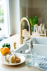 Plate with an ecobrush for washing dishes near the sink, soap in a glass bottle, a towel.