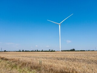 Wind turbine on dry field under clear blue sky. Concept of clean energy, rural landscape. single...