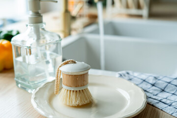 Plate with an ecobrush for washing dishes near the sink, soap in a glass bottle, a towel.
