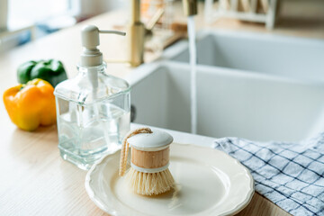 Plate with an ecobrush for washing dishes near the sink, soap in a glass bottle, a towel.