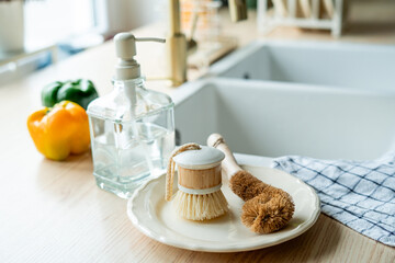 Plate with an ecobrush for washing dishes near the sink, soap in a glass bottle, a towel.