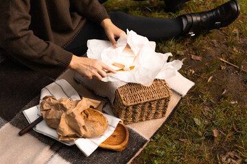 A rustic picnic moment as female hands butter fresh bread on a checkered blanket beside a wicker basket.