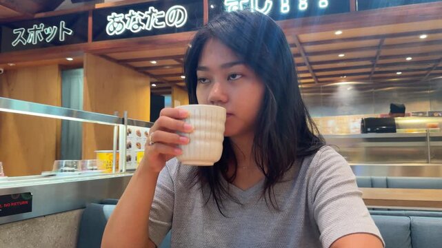 A Young Asian Woman Enjoys Warm Ocha Tea in a Cozy Japanese Restaurant Interior.