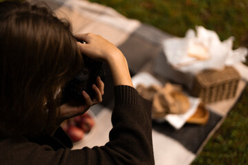A female photographer capturing cozy picnic scenes in a golden autumn landscape surrounded by trees.