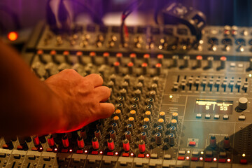 Close-up of a sound engineer's hand adjusting controls on a professional audio mixing console...