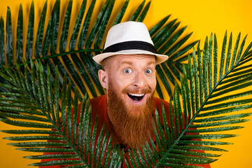 Cheerful young man wearing a white hat smiling amidst tropical leaves with a vibrant yellow...