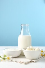 Fresh dairy products and flowers on white wooden table against light blue background