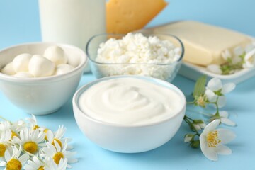 Fresh dairy products and flowers on light blue background, closeup