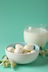 Fresh milk in glass, mozzarella balls and flowers on turquoise background, closeup. Dairy products