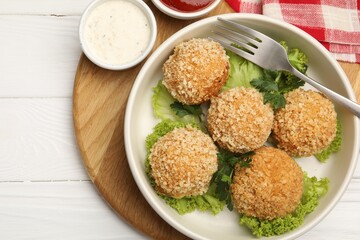 Delicious fried croquette balls with parsley, lettuce and sauces on white wooden table, top view