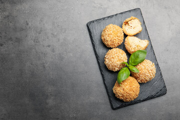 Delicious fried croquette balls with basil on grey textured table, top view. Space for text