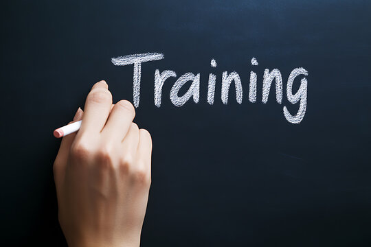 Writing "Training" on a chalkboard with chalk to symbolize education, learning, development, or professional growth.