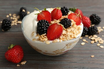 Tasty yogurt with granola and berries in bowl on wooden table, closeup