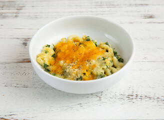 Macaroni with Kale and Melted Cheese in bowl on wooden table side view of comfort food