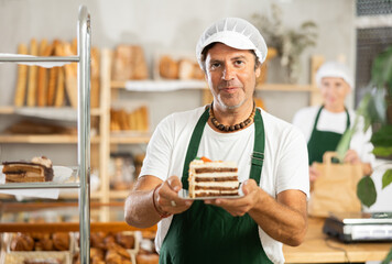 During working day, bakery male employee takes piece of cake out of window, shows and advertises...
