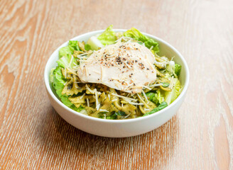 Chicken Pesto Farfalle Pasta Salad with Fresh Greens and Parmesan Cheese in bowls on wooden background side view of Italian cuisine