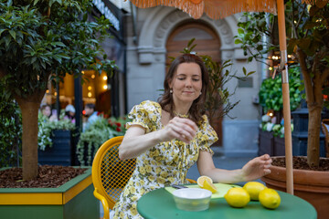 A woman in a floral dress sips a lemon-flavored beverage at an outdoor cafe, surrounded by lush greenery and vibrant colors