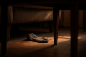 Single sock lying on wooden floor under a chair in a cozy indoor setting with warm light