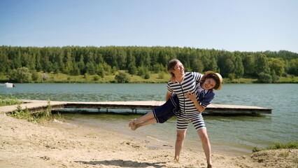 Happy couple wearing vintage striped swimsuits playfully lifting each other on a sunny beach by the lake