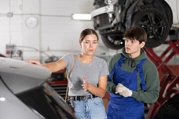 Girl who owns car talks about problems to an auto mechanic at a car service center