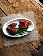 Crispy fried chicken wings garnished with curry leaves on a white dish, beautifully presented on a rustic wooden background with a burlap napkin, creating a cozy and appetizing dining scene.