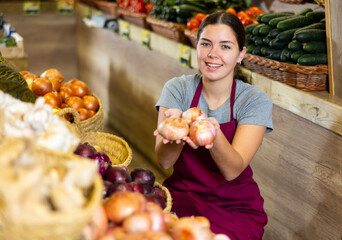 Female grocery store worker arranges red onion and other vegetables on the counter and display case
