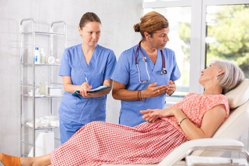 Elderly woman sitting in chair at clinic reception and carefully answers male doctor questions...