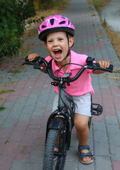 small brave boy of three years old in a helmet rides a bicycle in the city by himself