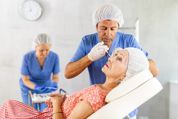 Elderly woman getting injections of hyaluronic acid in cheeks to correct facial contours and smooth...