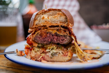 Cross section of juicy gourmet bacon cheeseburger with melted cheese, fresh vegetables, and toasted bun served with craft beer in casual restaurant setting