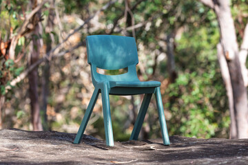 Photograph of a small green plastic recreational chair that has been abandoned or forgotten on a large flat rock amongst trees in a forest in NSW, Australia.