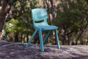 Photograph of a small green plastic recreational chair that has been abandoned or forgotten on a large flat rock amongst trees in a forest in NSW, Australia.