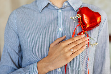 Woman holding heart balloon with engagement ring. Close-up of woman in striped shirt holding red...