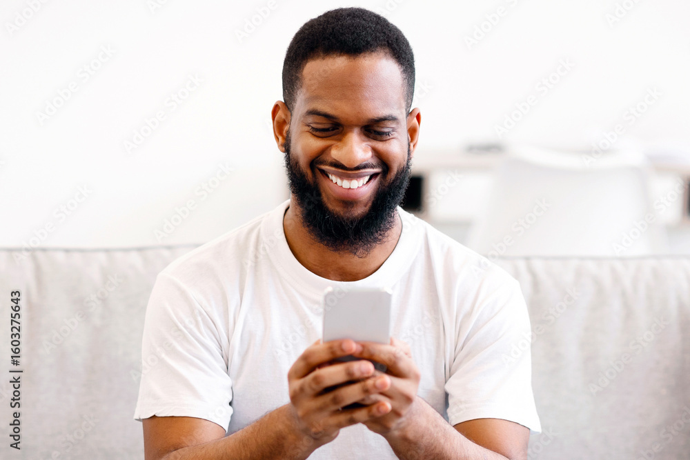 Poster african guy using smartphone texting and browsing internet, networking in social media sitting on so