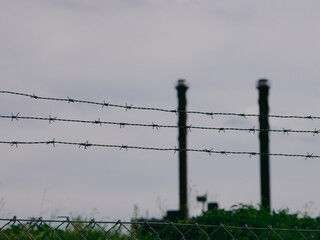 Barbed wire in front of industrial chimneys.