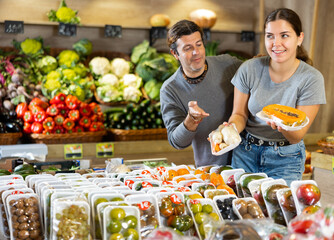 Family couple with purchases of fresh vegetables and fruits in supermarket