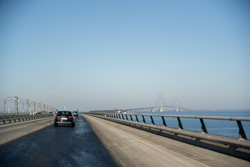 Driving Over Great Belt Bridge: Majestic Cable-Stayed Bridge Spanning Blue Waters Under Clear Sky...