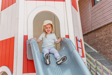 Cute girl child in panama rides a slide on a playground.