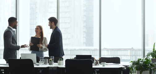 Businesspeople talking in office, standing against window by table, panorama, copy space