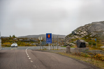 Norway Border Crossing: Remote Arctic Road Entering Rugged Nordic Landscape Under Overcast Skies...