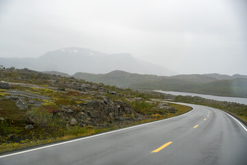 Misty Arctic Road Journey: Winding Highway Through Rocky Tundra, Lakeside Views, and Hazy Mountains Under Grey Sky