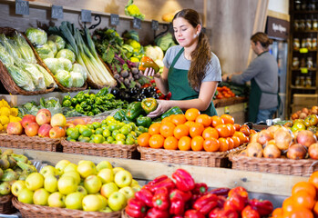 Young woman in apron sells bell pepper in vegetable shop