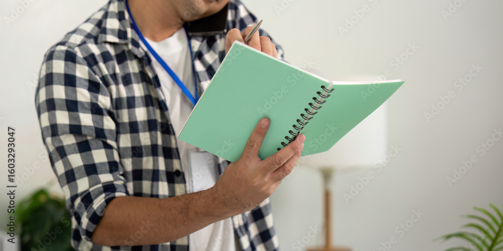 Poster note taking. young professional writing in a notebook while on a phone call.