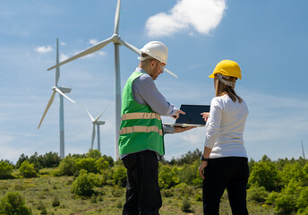 Two engineers working on a wind turbine field with a laptop