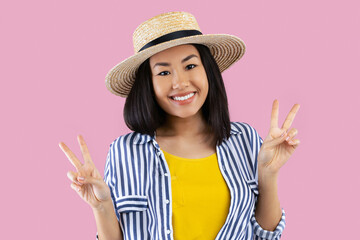 Having Fun. Portrait of a smiling happy asian woman in straw hat showing two victory sign or peace...
