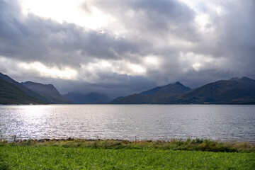 Dramatic Fjord Landscape: Shimmering Waters & Cloudy Mountains Under Nordic Sky – Perfect for...