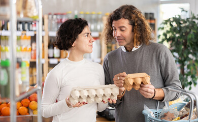 Married couple chooses eggs in a supermarket. Husband and wife buying farm eggs at a grocery store