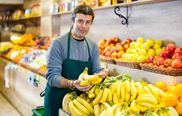Positive male seller with ripe bananas on the supermarket