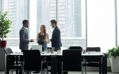 Coffee break. Businesspeople talking in front of office window after meeting, standing by table,...